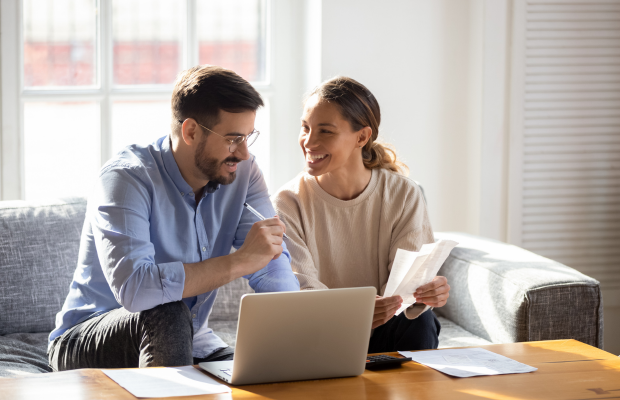 a man and woman sitting on a couch looking at a laptop