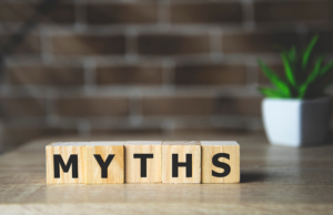 Wooden blocks spelling "MYTHS" on a table with a blurred plant behind.