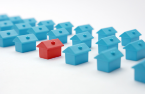 A vibrant red house contrasts sharply with a row of blue houses in a picturesque neighborhood setting.