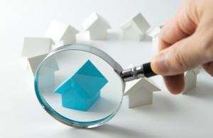 Small houses on coins with a magnifying glass highlighting details.