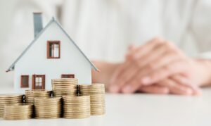 a woman sitting at a table with stacks of coins and a house