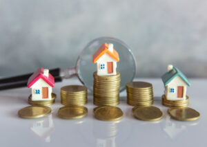 Small houses on coins with a magnifying glass highlighting details.