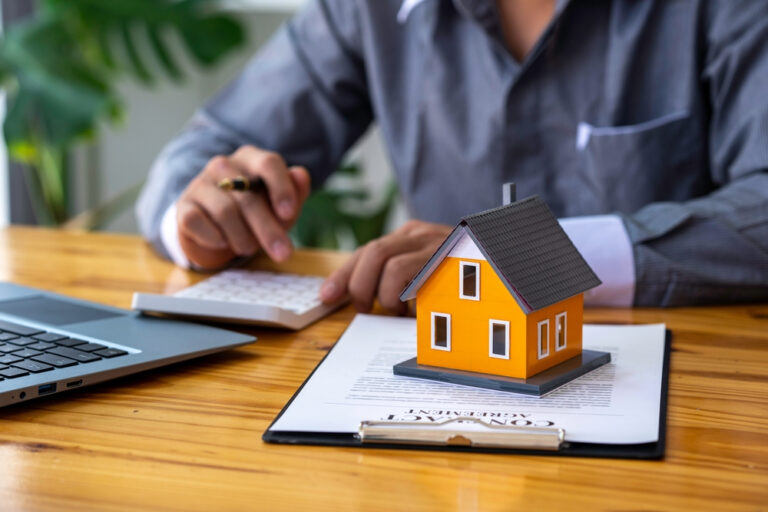a man sitting at a desk with a laptop and a model of a house