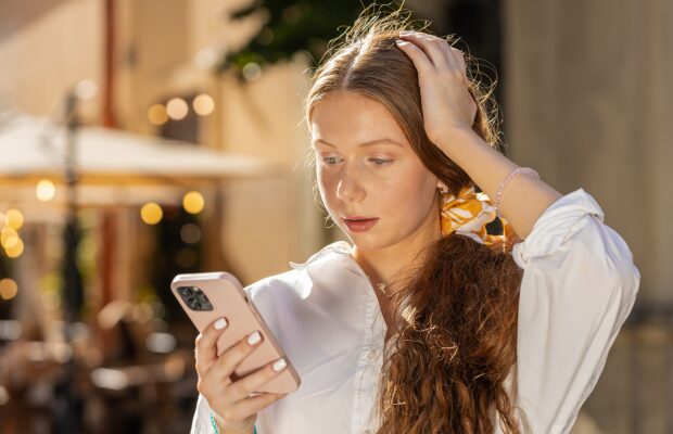 A woman stands outside, focused on her phone screen.