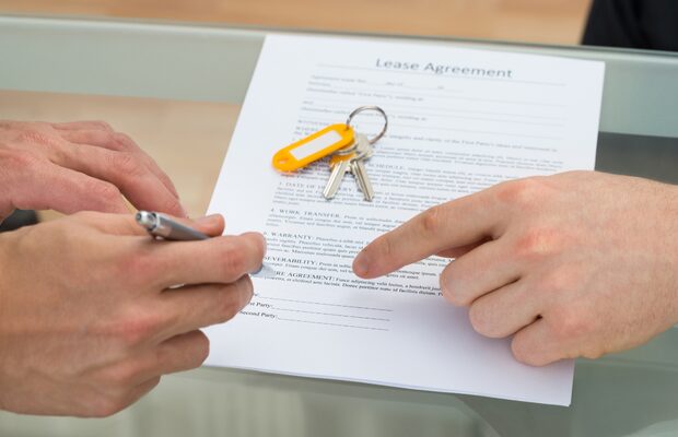 Close-up of hands signing a lease agreement with house keys placed on the document during a leasehold property sale