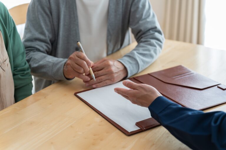 A man and woman sit at a table, writing notes with a pen and paper.