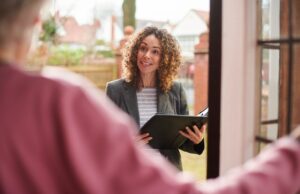 A landlord or estate agent speaking with a sitting tenant at the front door of a UK property, discussing the sale of the home while the tenant remains in residence