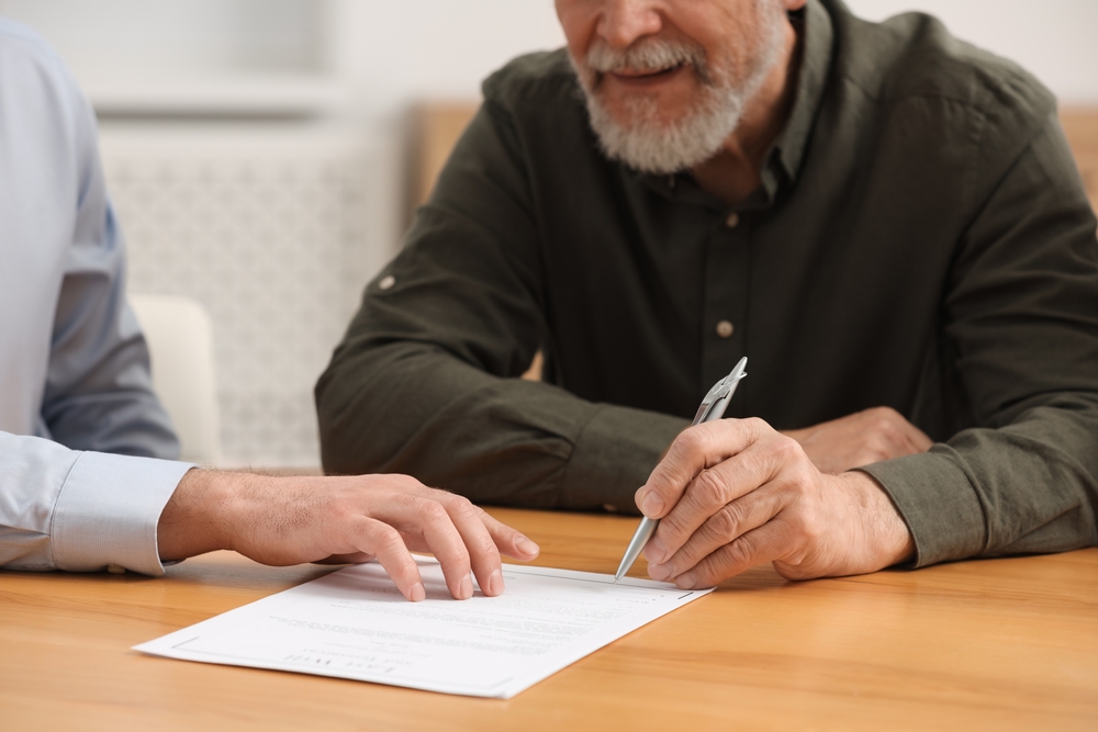 Two men signing documents at a table in a professional setting.