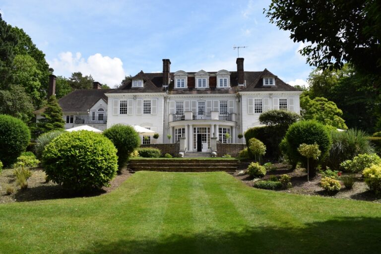 A large white house surrounded by a lush garden and lawn.