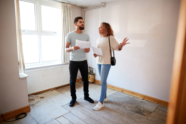 A man and woman stand together in a vacant room.