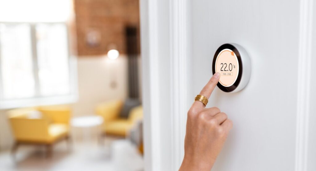 Hand adjusting a smart thermostat in a modern London flat to save on winter energy bills.