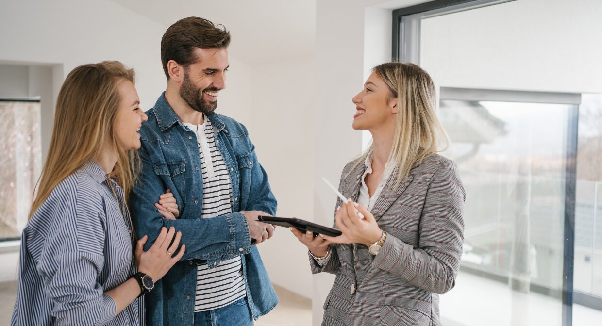 A smiling estate agent discussing a property sale with a couple during a viewing, representing Ellis & Co’s 2025 guide to selling homes faster in a competitive market.