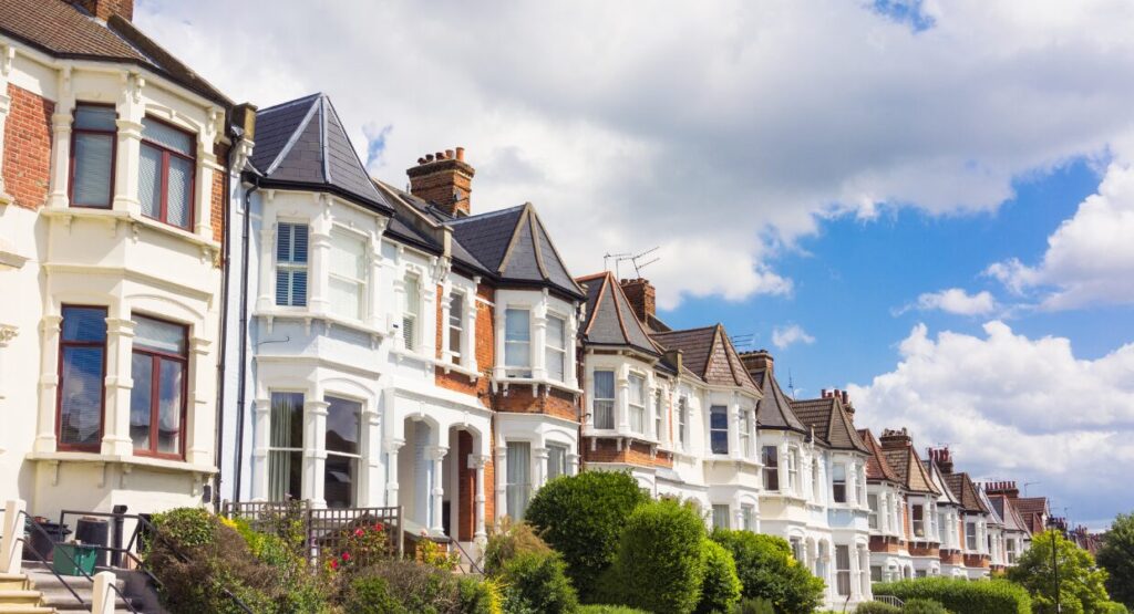 A row of well-kept terraced houses on a residential street with greenery and bright clouds, representing the strong demand for rental properties in 2025.