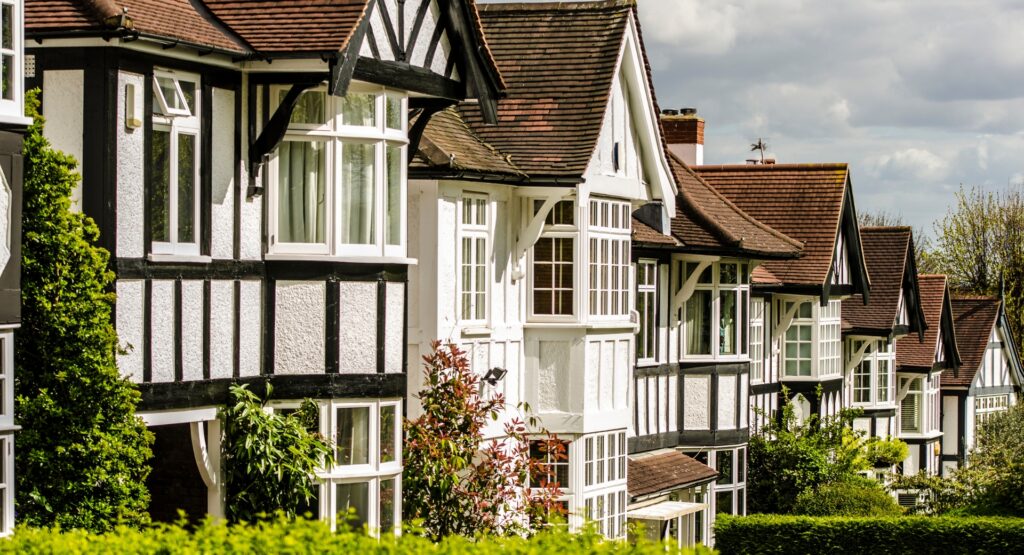 Row of traditional UK period houses with Tudor-style features, bay windows and pitched roofs on a residential street.