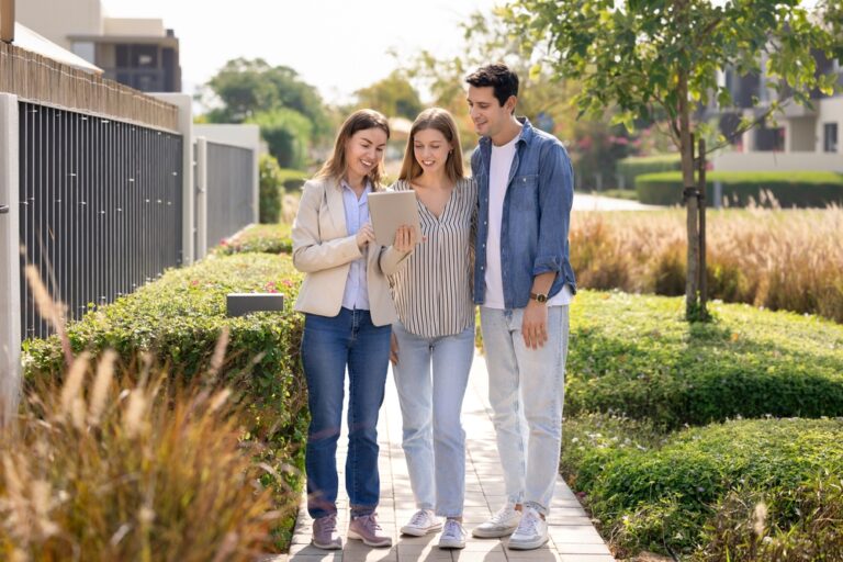 Three people on a sidewalk, collaborating on a tablet together.