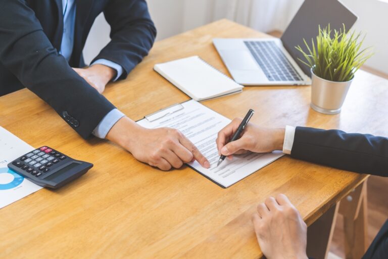 Two business people signing a contract at a desk.