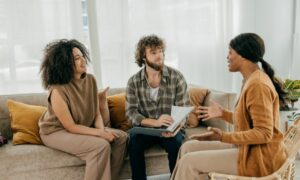 A couple sitting on a sofa discussing paperwork with a professional during a relaxed meeting in a modern living room.