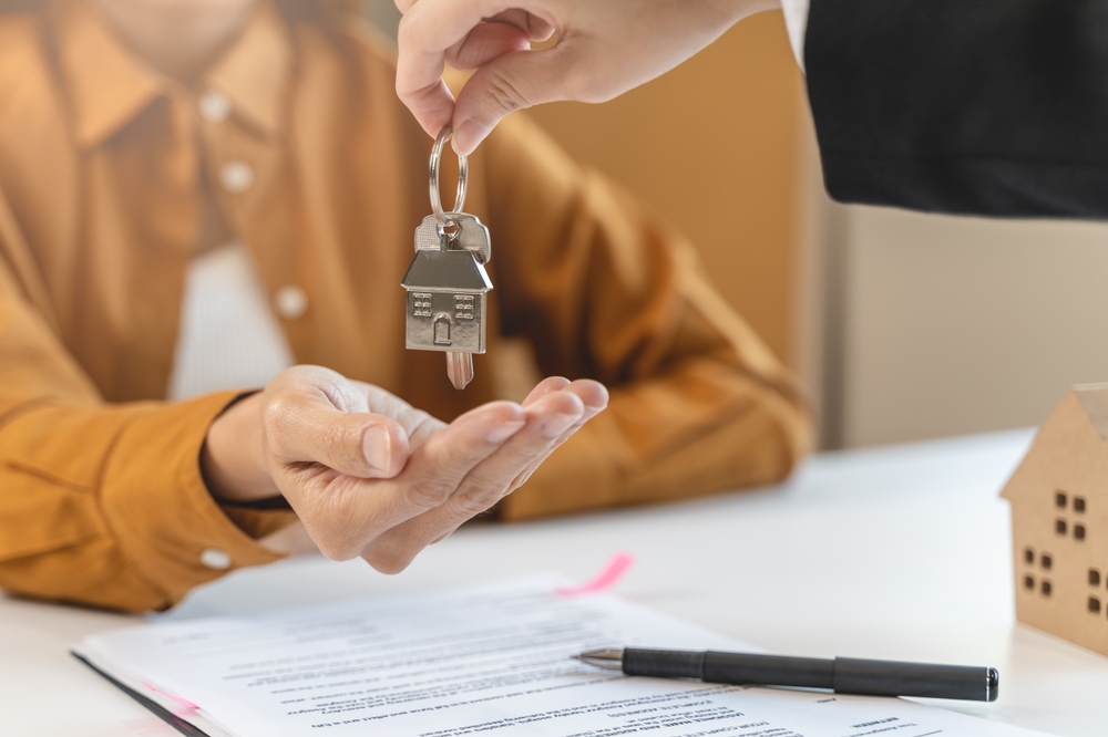 A person hands a house key to another person at a desk.