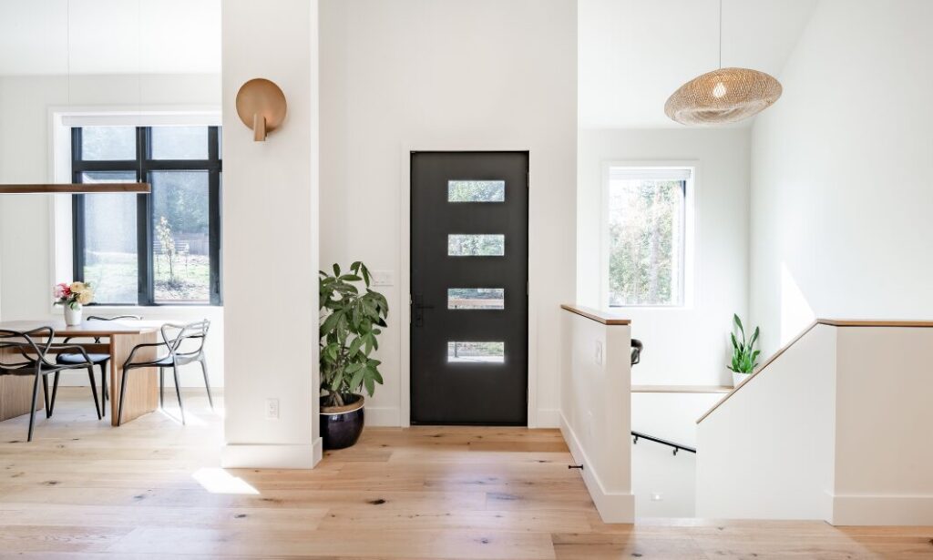 Bright modern entrance hallway with black front door, wooden flooring, indoor plants and a dining area in a contemporary Tonbridge home.