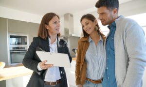 Estate agent talking with two potential buyers during a property viewing inside a modern kitchen.
