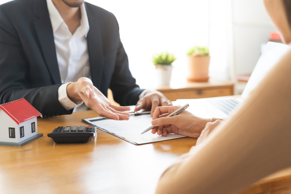 Real estate agent showing a house to a couple in a bright living room.