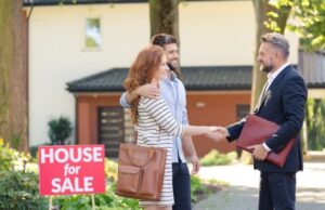 Couple shakes hands with real estate agent by for-sale sign.