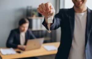 A man stands holding a key, symbolizing ownership of a house.