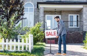 Man placing “SALE” sign in front yard of suburban brick house