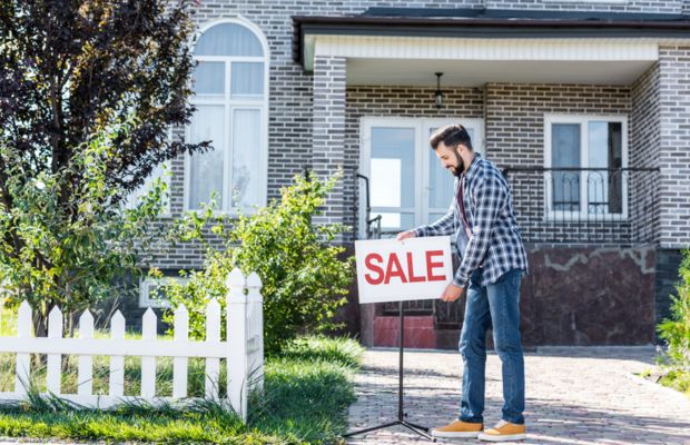 Man placing “SALE” sign in front yard of suburban brick house