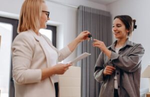 Two women exchanging keys in an indoor setting.