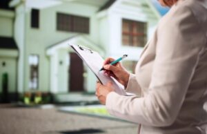 A woman writes on a clipboard while standing in front of a house, focused on her task.