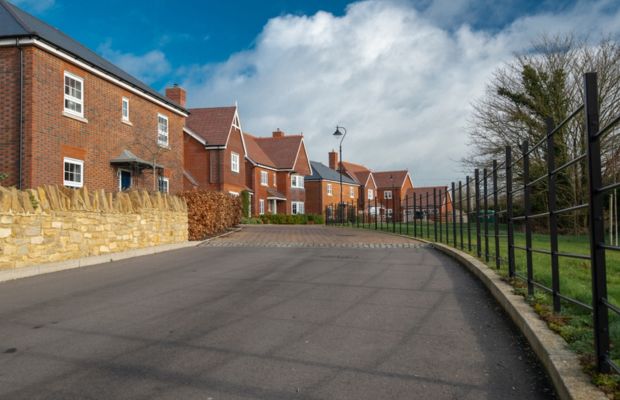 A road lined with a fence and residential houses on both sides, showcasing a suburban neighborhood.