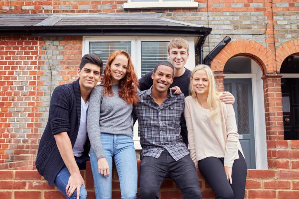 Group of young adult tenants outside a brick shared rental house during the summer.