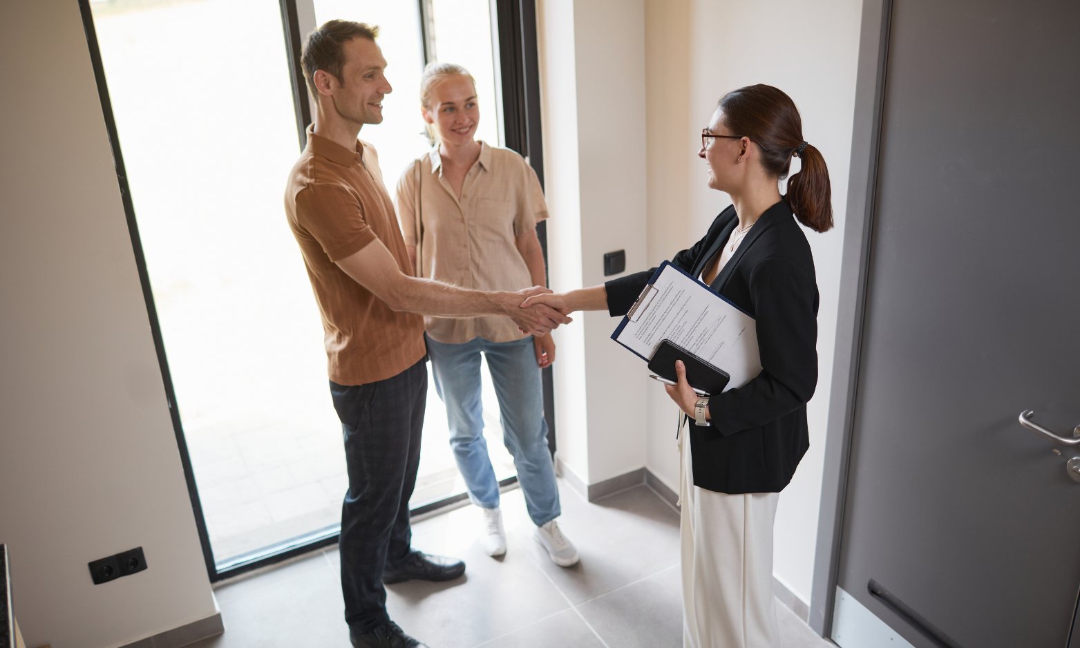 Estate agent greeting a couple inside a bright modern home