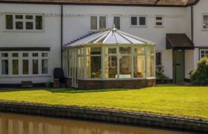 A white house with a glass conservatory extension overlooking a grass lawn and a canal.